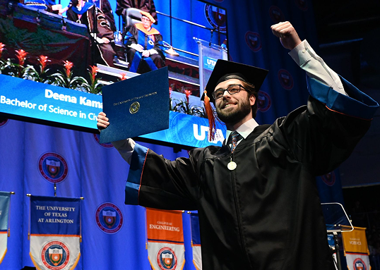 Graduate in cap and gown at university graduation ceremony with branded displays